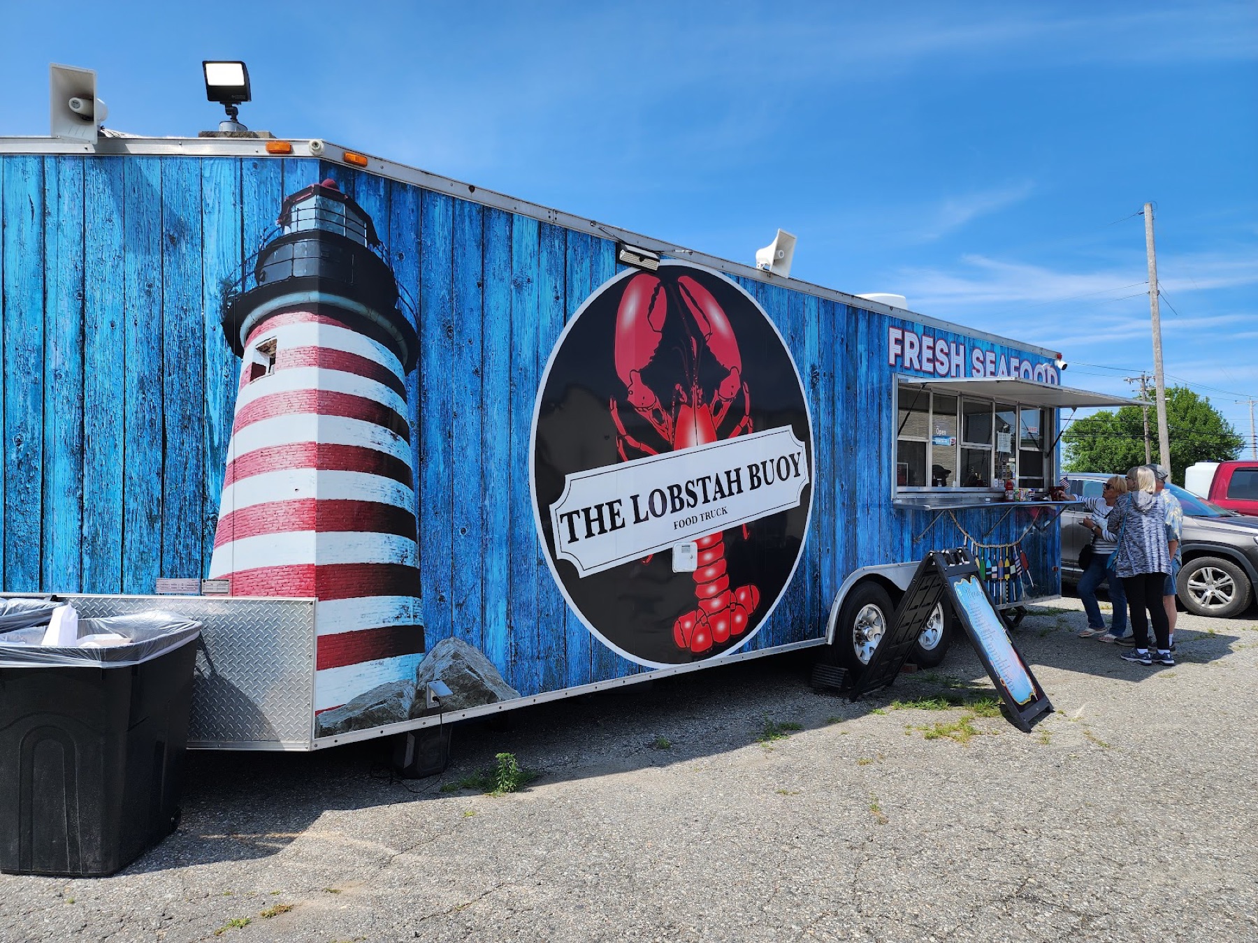 The blue Lobstah Buoy trailer with its red lobster and lighthouse mural, customers ordering at the window.